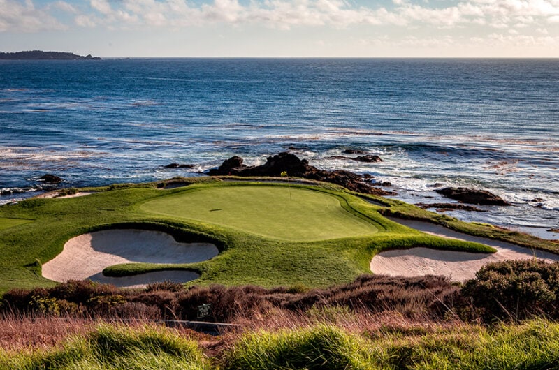 Exterior photo of hole 7 at Pebble Beach Golf Course surrounded by the ocean and sunny skies.